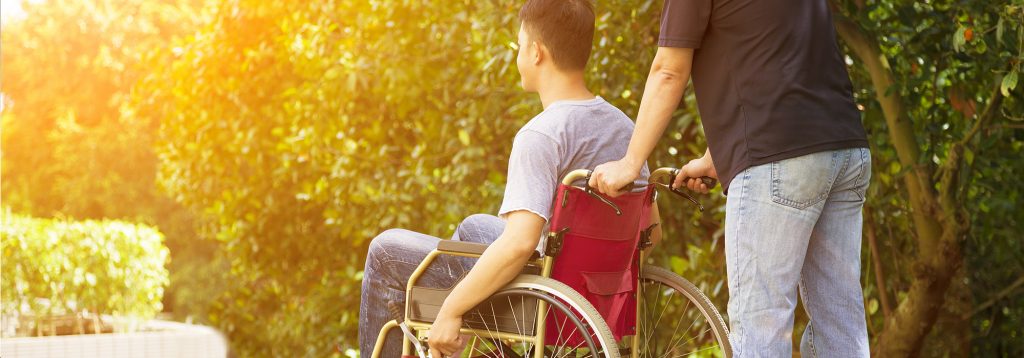 family caregiver pushes man in wheelchair after catastophic injury
